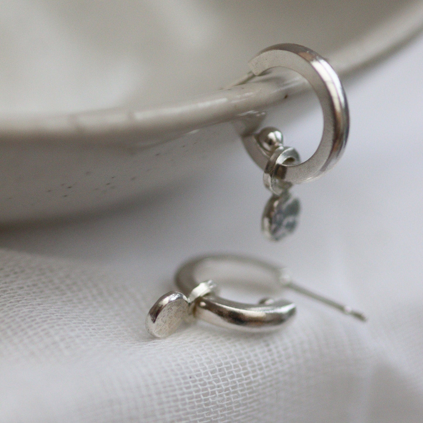 Silver huggie hoops with confetti like circular hammered drops.
