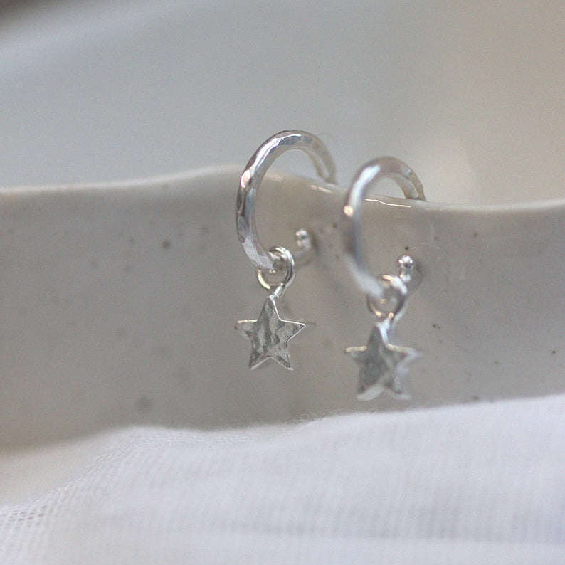 Silver hoop earrings with star charms on a white surface