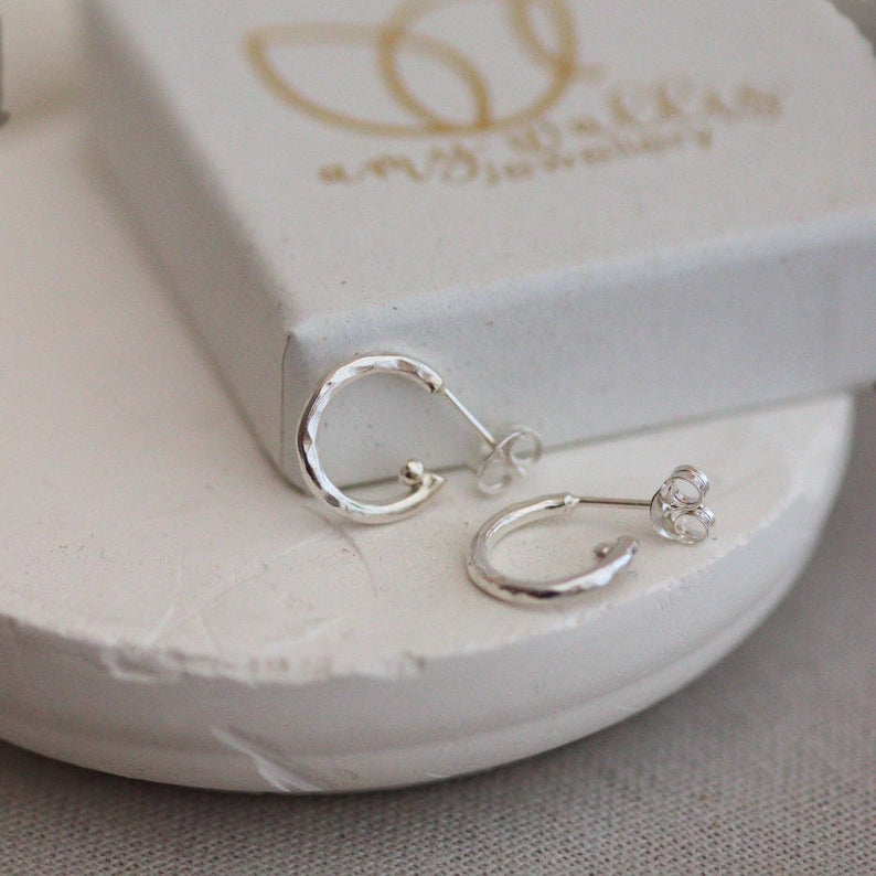 Silver earrings on a white stand with 'Amy Dally' branding in the background