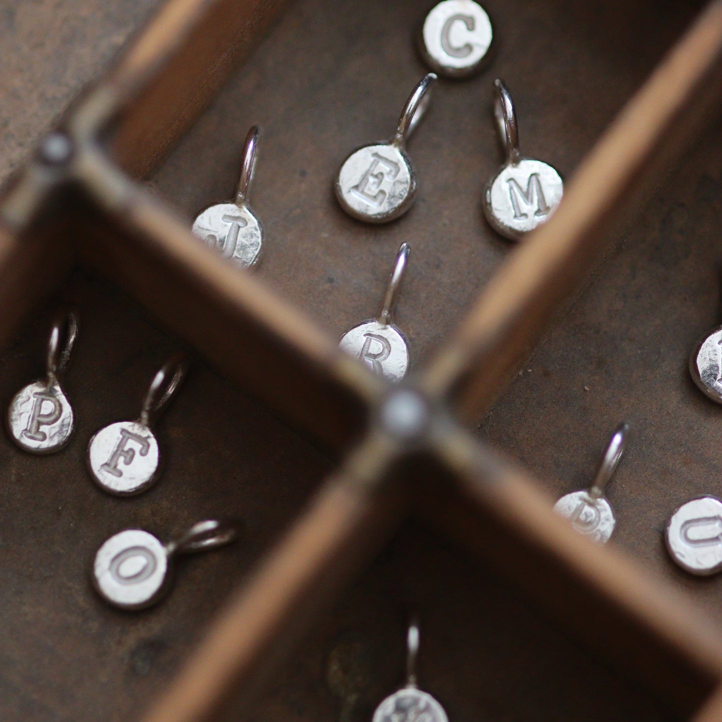Silver pebble pendants with engraved letters in a wooden letterpress tray.