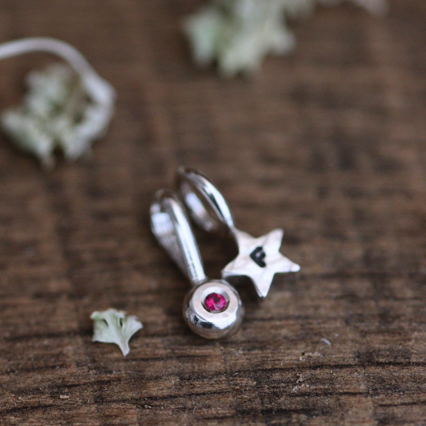 A red birthstone pendant and star pendant on a wooden background.
