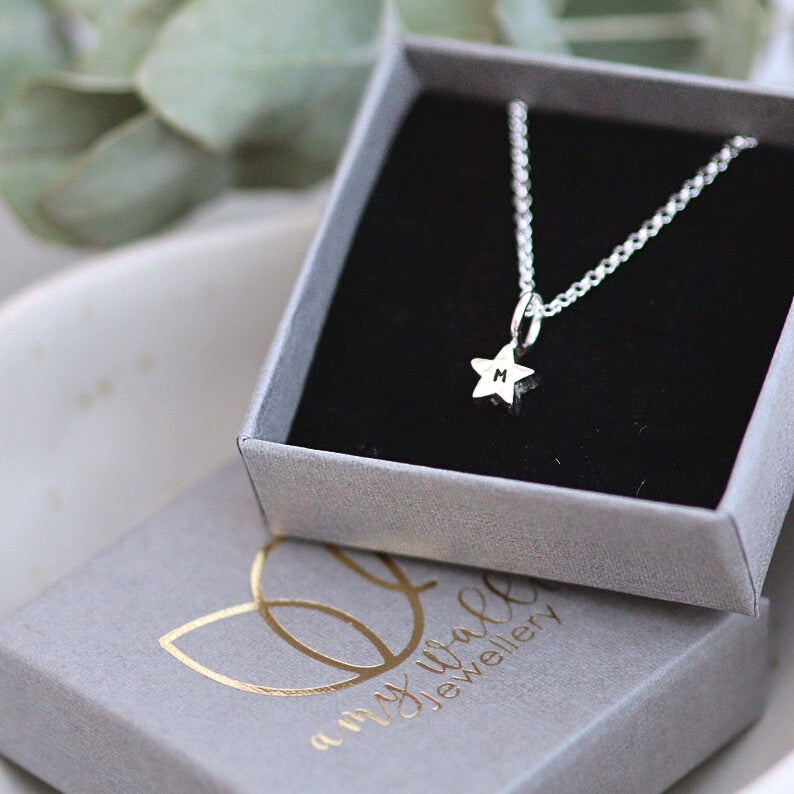 Silver star charm on a fine silver chain with a letter m personalisation. In a grey branded box.