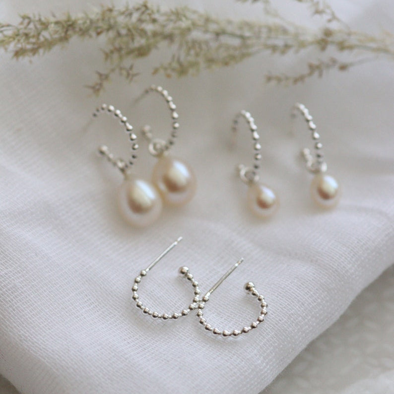 silver beaded hoop earrings with no pearls, large pearl drops and small pearl drops on a light background.