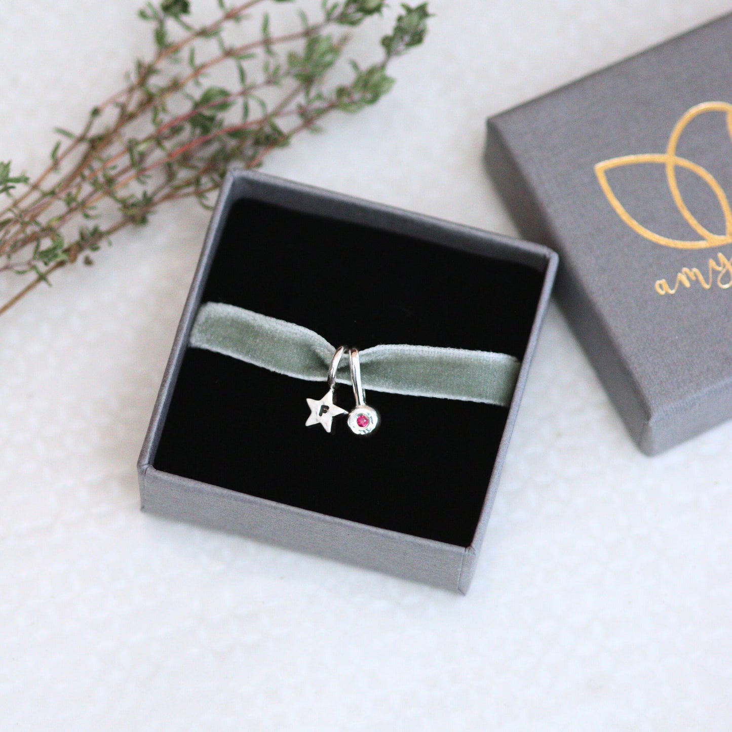 silver star charm on a green velvet ribbon in a jewellery box on a light background.