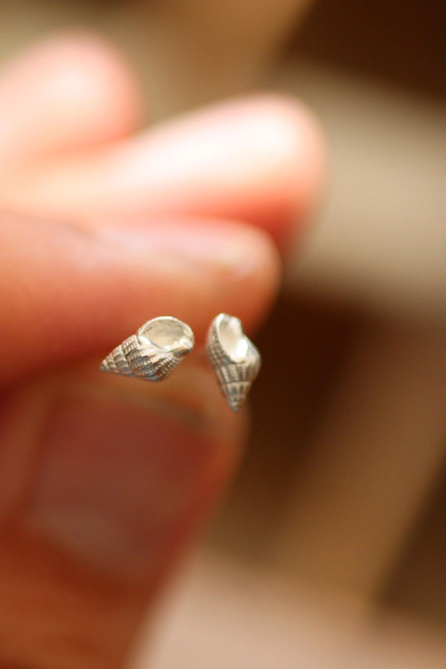 Silver shell-shaped earrings held between fingers with a blurred background.
