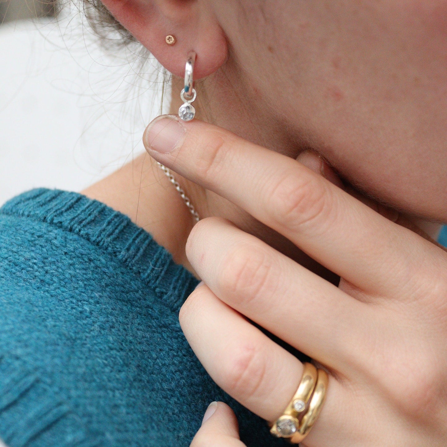 silver huggie hoops being worn with a hammered disc drop.