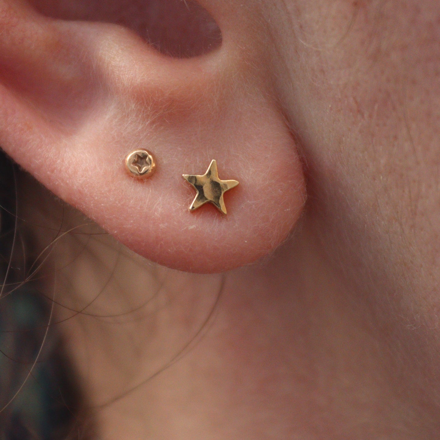 Tiny gold star studs in an ear lobe with tiny star dots in the second piercing.