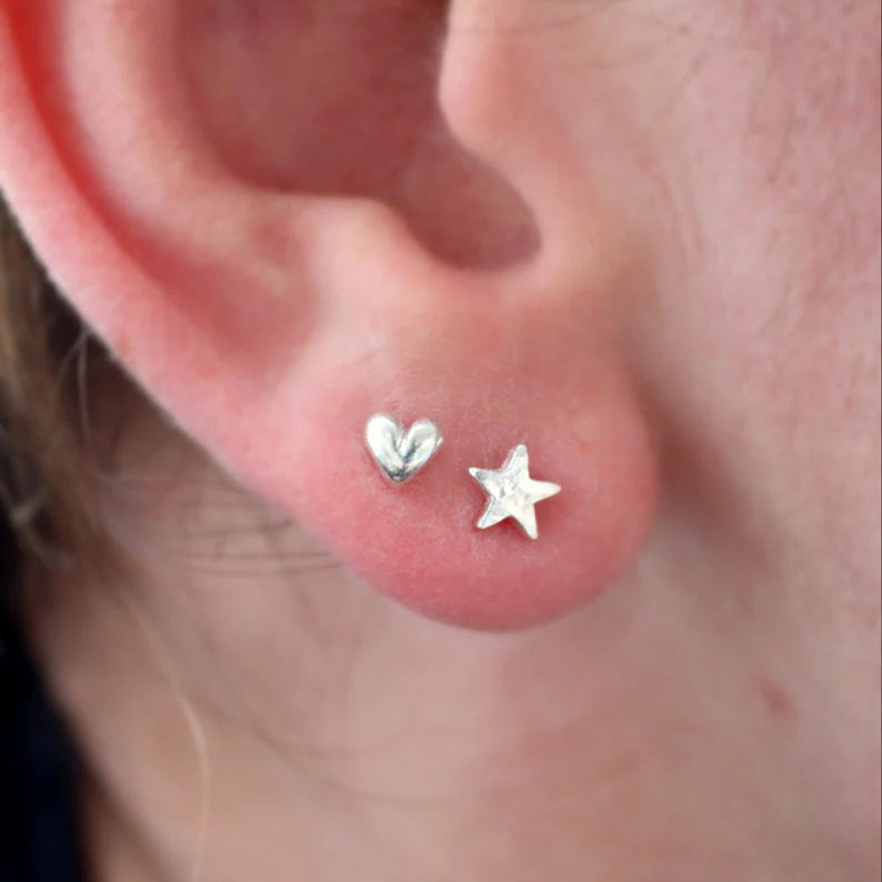 A tiny star stud next to a tiny heart stud in an ear lobe being worn.