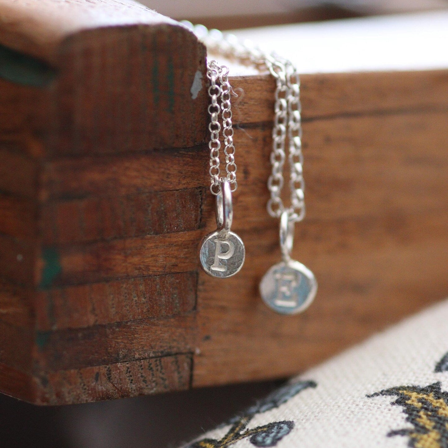 Silver pebble pendants on a silver chain against a wooden tray.