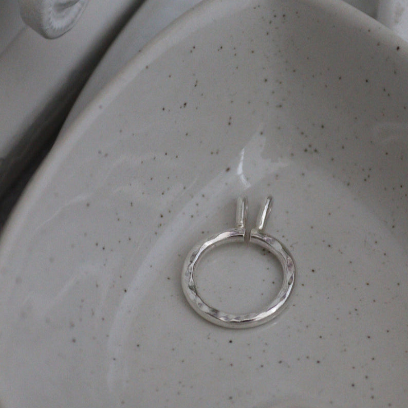 A silver keeper pendant with hammered finish on its own in a heart shaped bowl.
