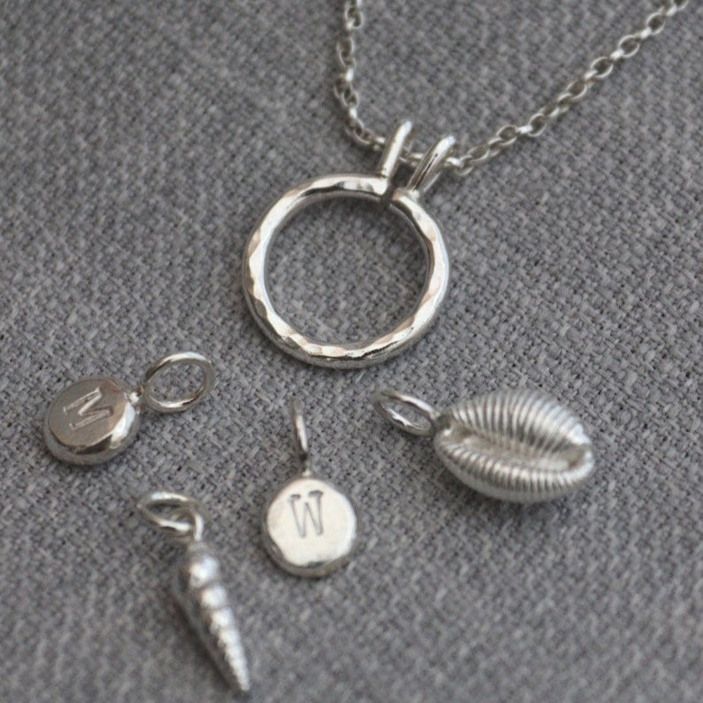 A sterling silver keeper pendant that looks like a hammered ring on a chain with silver charms that can be worn attached to the ring.