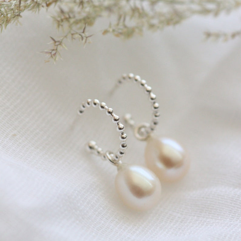 Pearl hoop earrings on a soft white background with delicate greenery