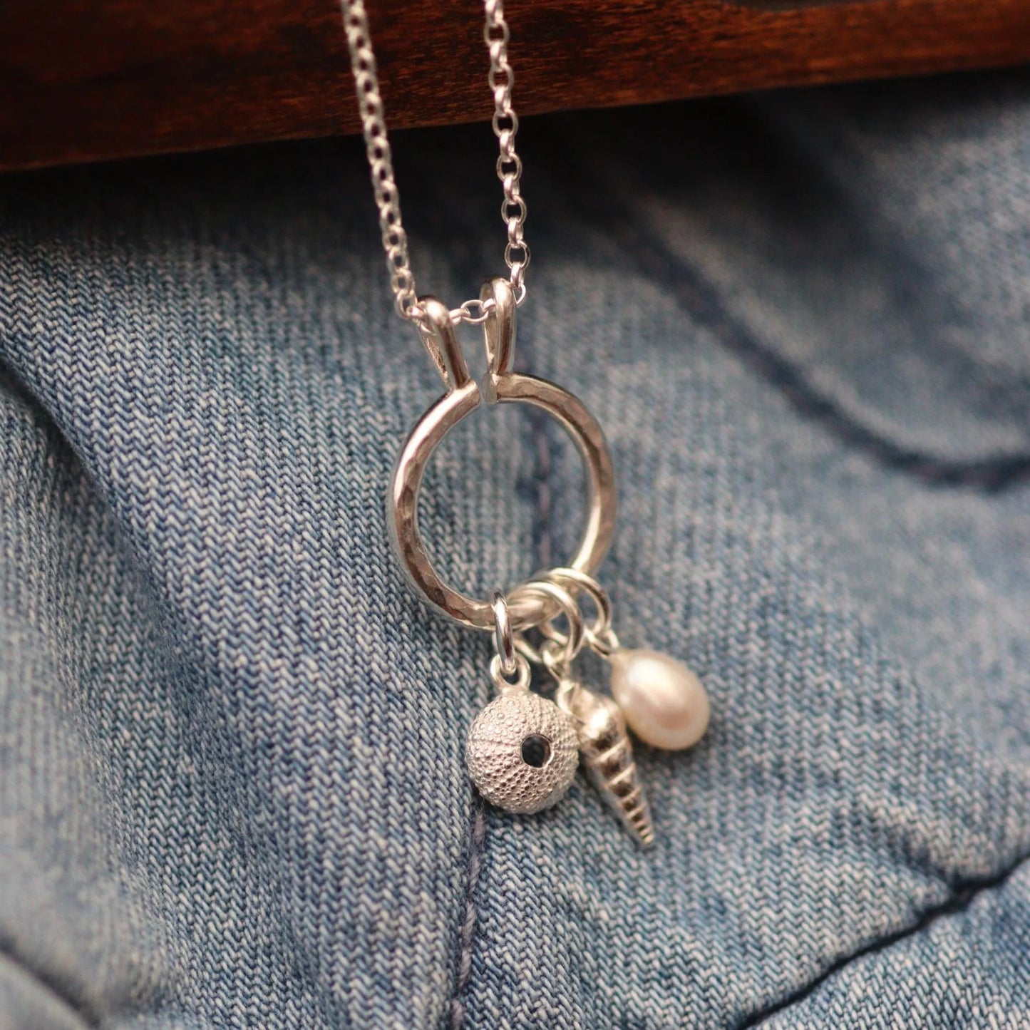 a silver keeper necklace with various charms including a pearl, spiral shell and sea urchin. It looks like a modern charm necklace.