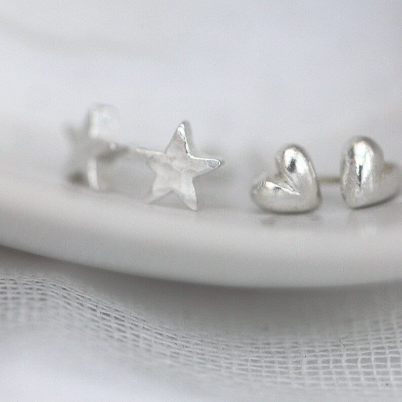 tiny silver heart and star studs next to each other on the edge of a plate, They are the same size.