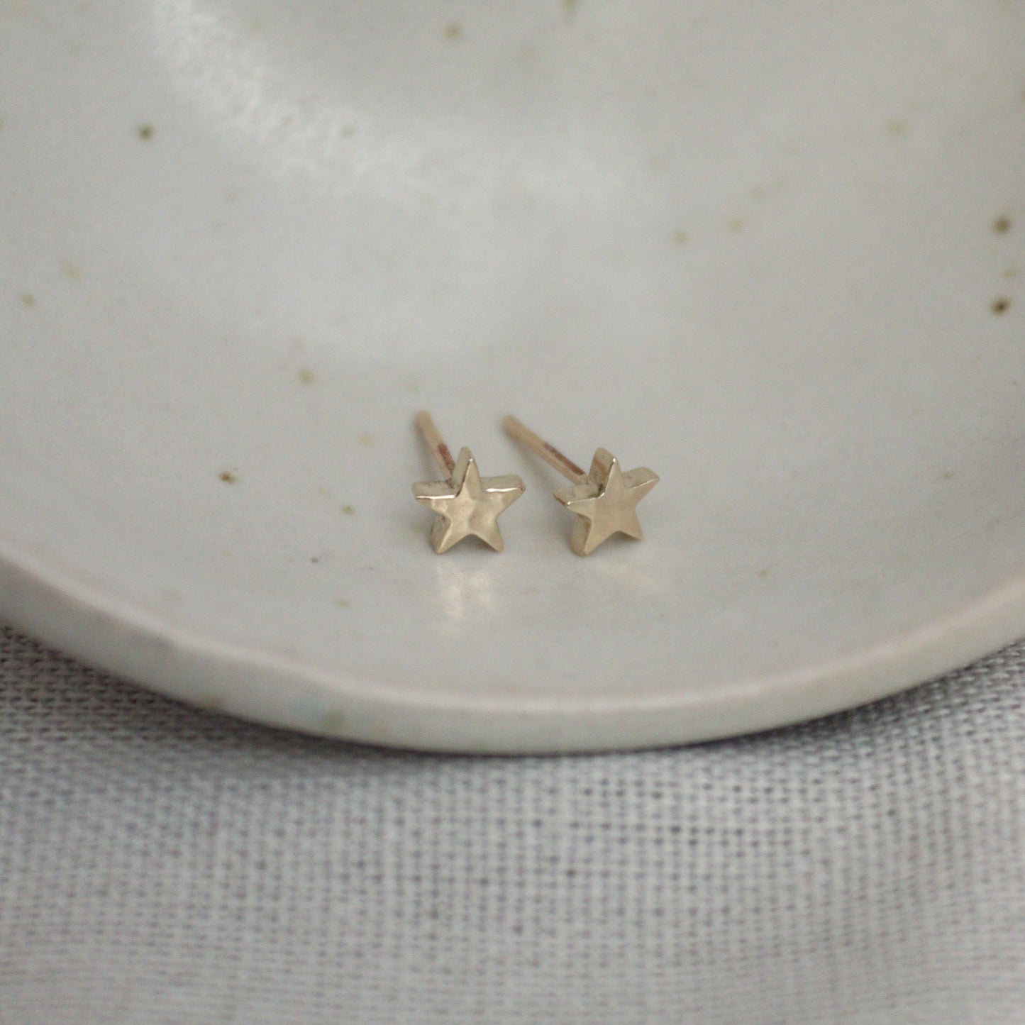 Little 9ct yellow gold star studs on a white bowl. The studs have a hammered finish.