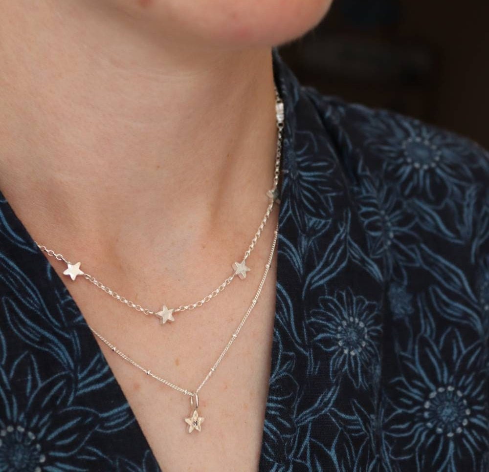 Two layered silver star necklaces on a model wearing a blue seasalt cornwall jumpsuit.