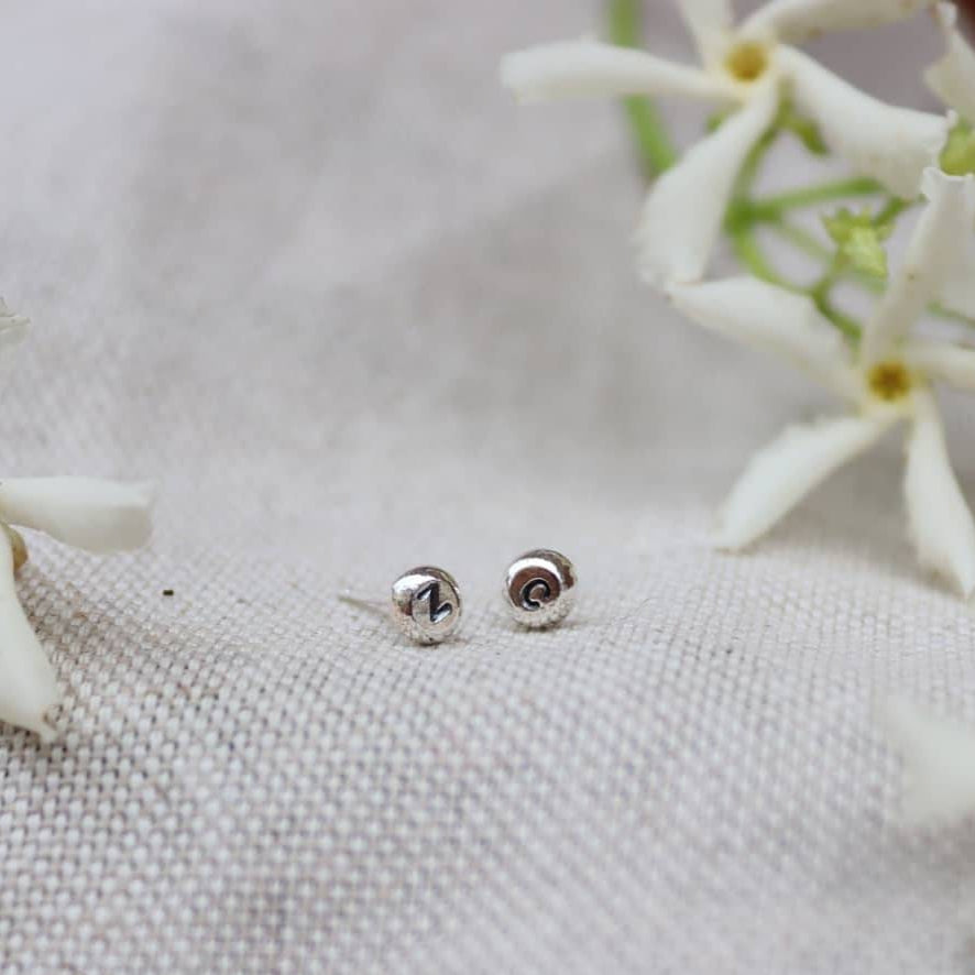 two stud earrings with a bright silver finish and initials stamped into them.