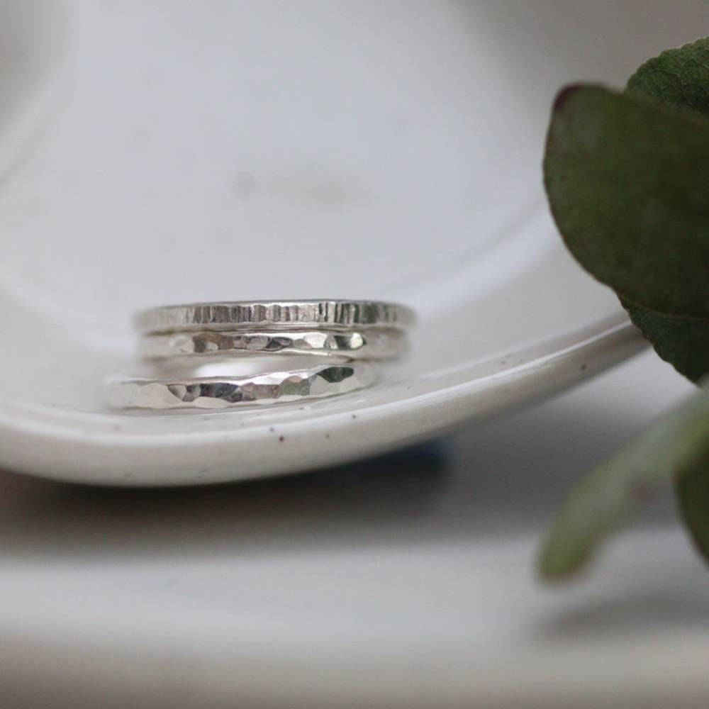 A stack of hammered and bark texture silver stacking rings in a bowl.