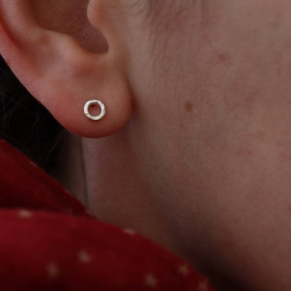 hammered silver hug stud in an ear against a red scarf.
