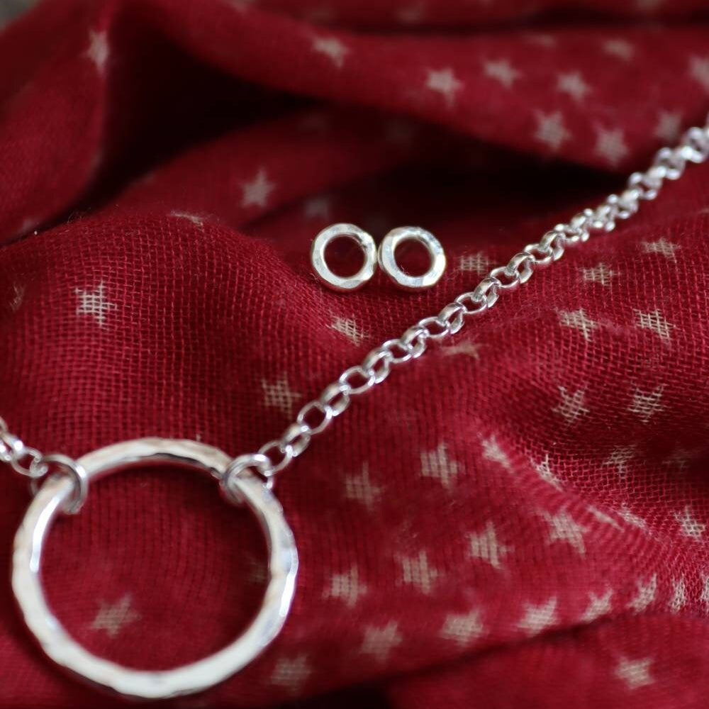 hammered silver circle studs next to a hammered eternity necklace on a red christmas scarf.
