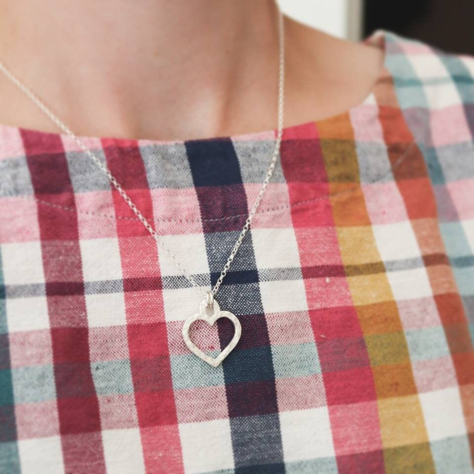 A silver heart necklace worn by a model in a plaid top from seasalt cornwall.