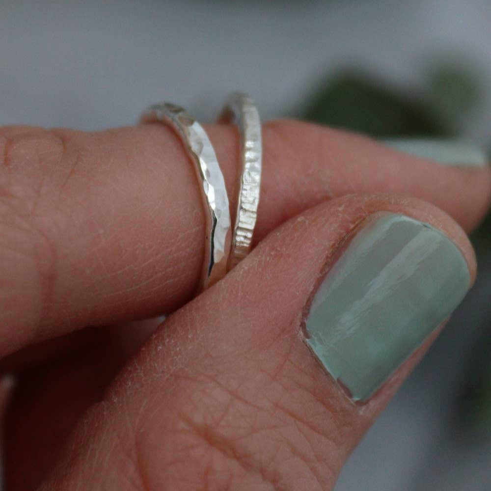 a hammered texture silver ring next to a bark texture ring with vertical ridges on a finger