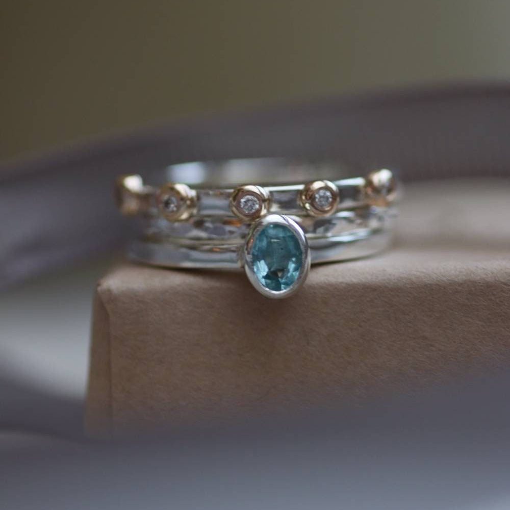 A stack of sterling silver rings one with an oval aquamarine, silver stacking ring and a silver and gold bobble ring with diamonds.