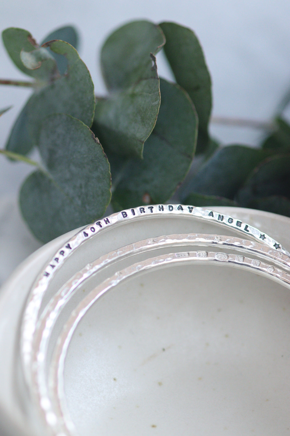 Silver bangles in a bowl with a personalised line of text stamped into one