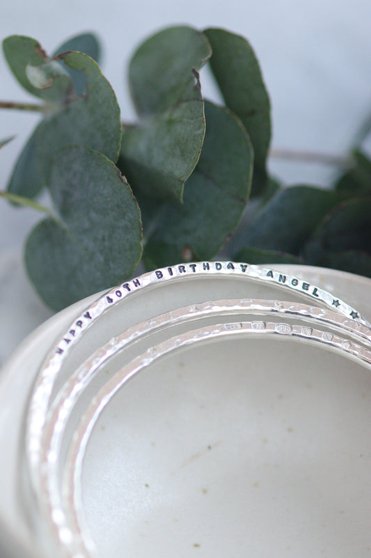 Silver bangles in a bowl with a personalised line of text stamped into one