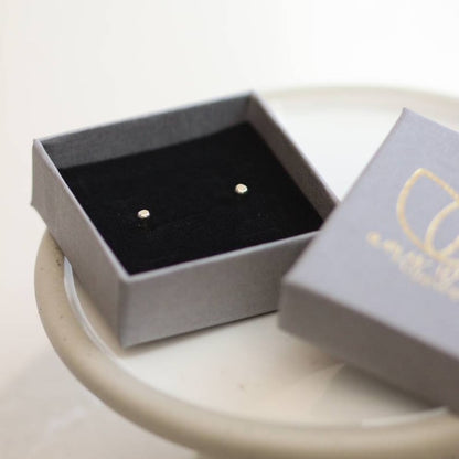 White gold tiny Earrings in an open grey jewellery box on a light surface