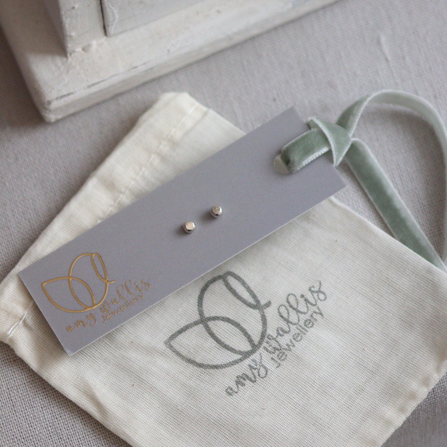 Small silver dot studs on a gray tag with a branded pouch in the background