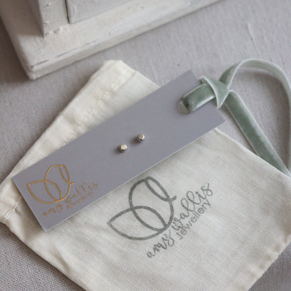 Small silver dot studs on a gray tag with a branded pouch in the background