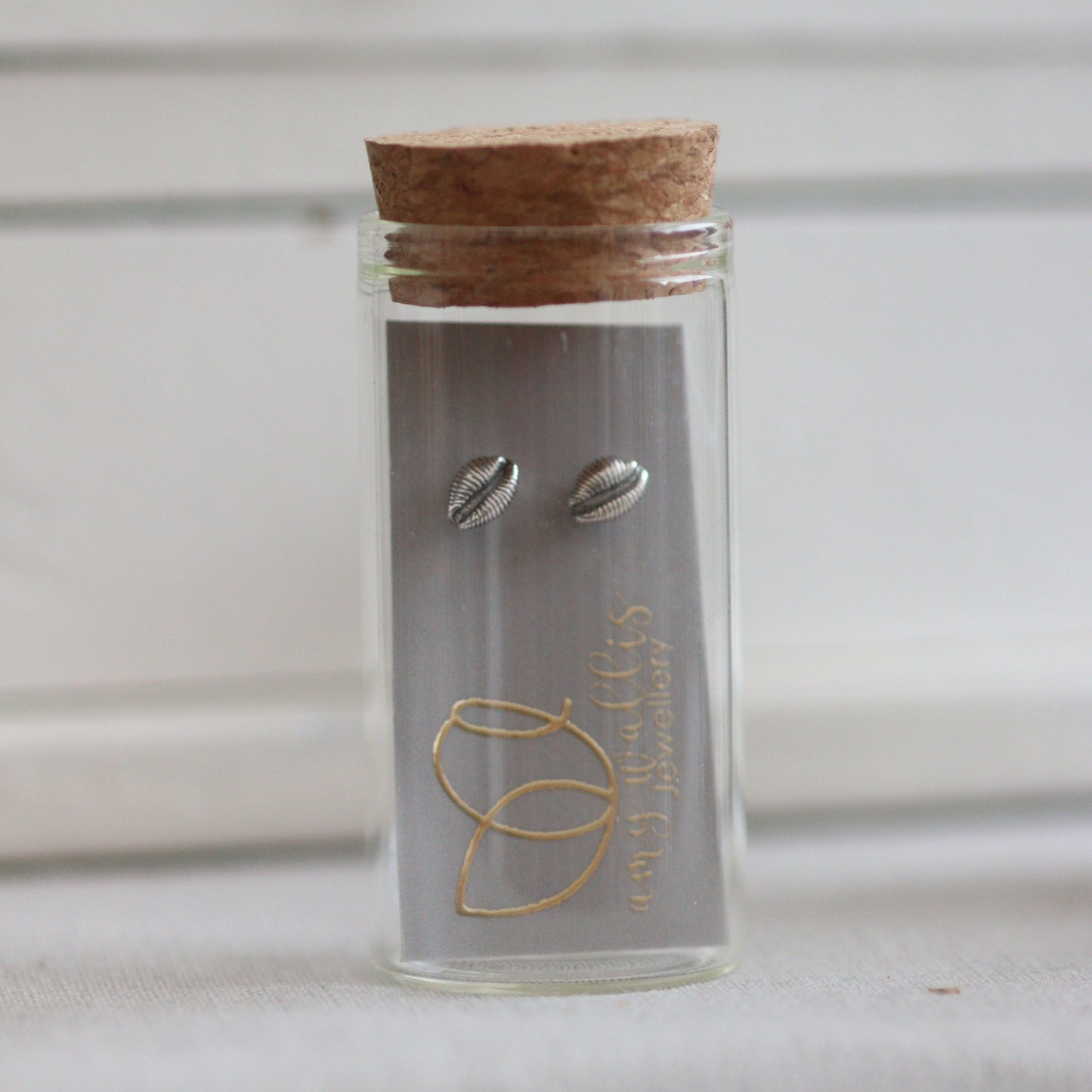 A glass bottle with cork and silver cowrie stud earrings inside.