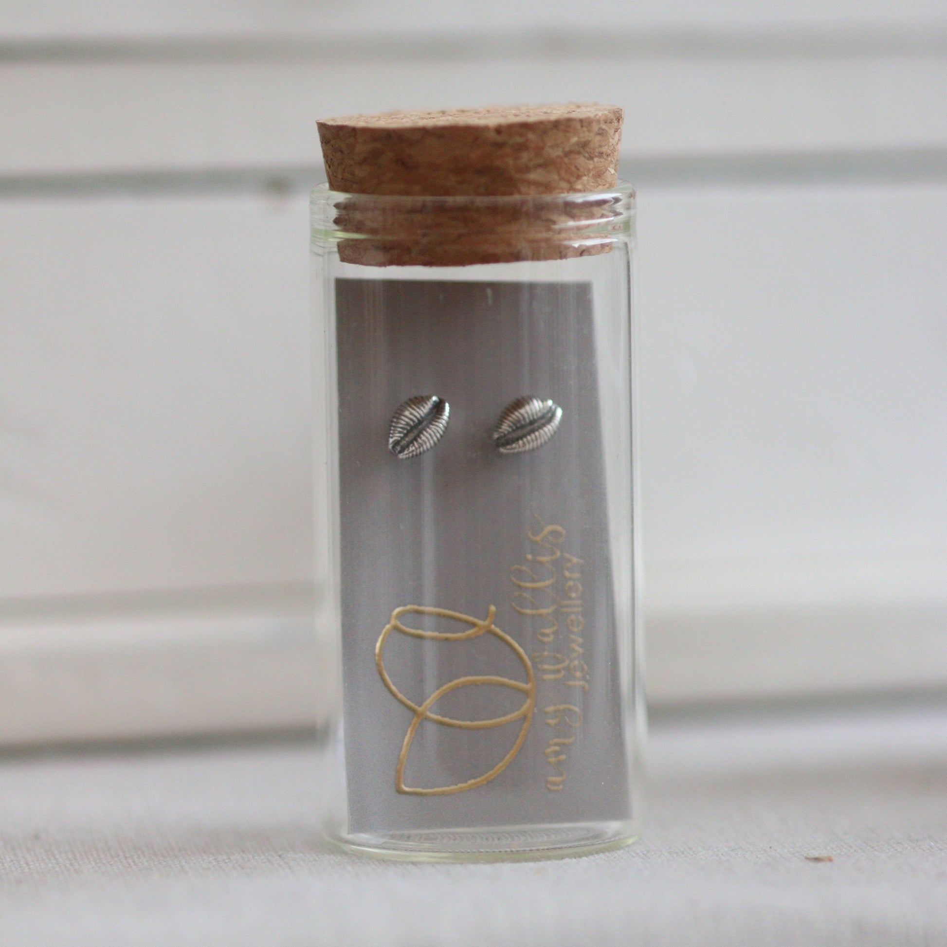 A glass bottle with cork and silver cowrie stud earrings inside.