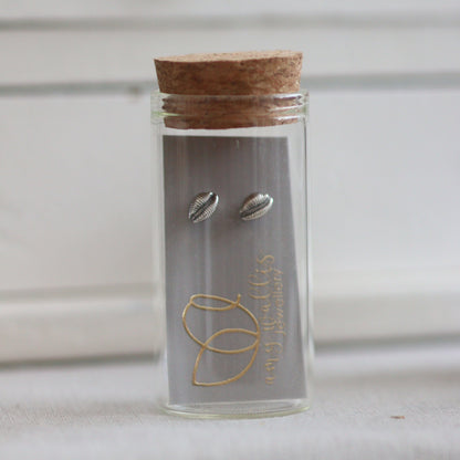 A glass bottle with cork and silver cowrie stud earrings inside.