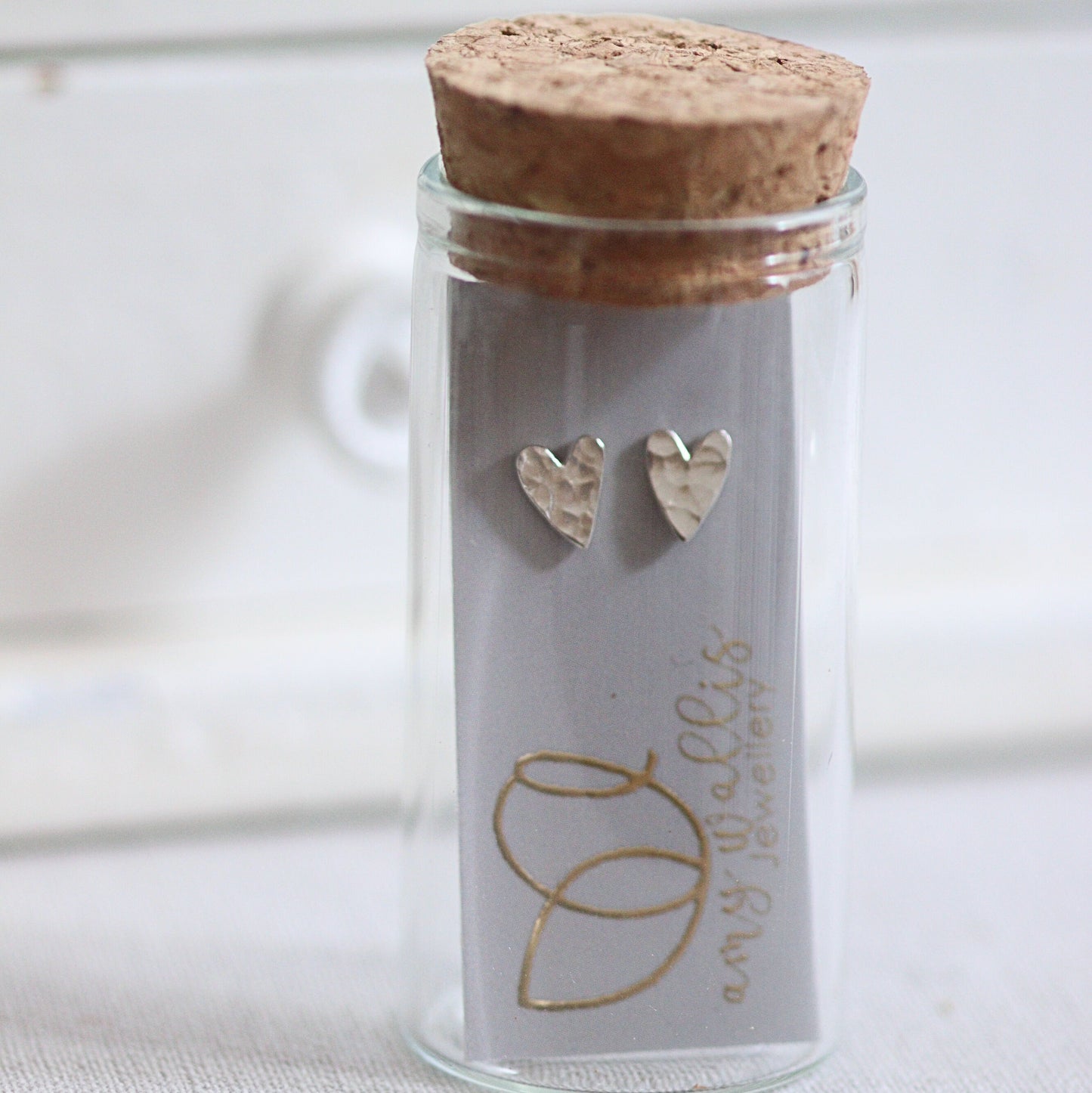 Glass jar with cork lid containing heart-shaped earrings on a white background