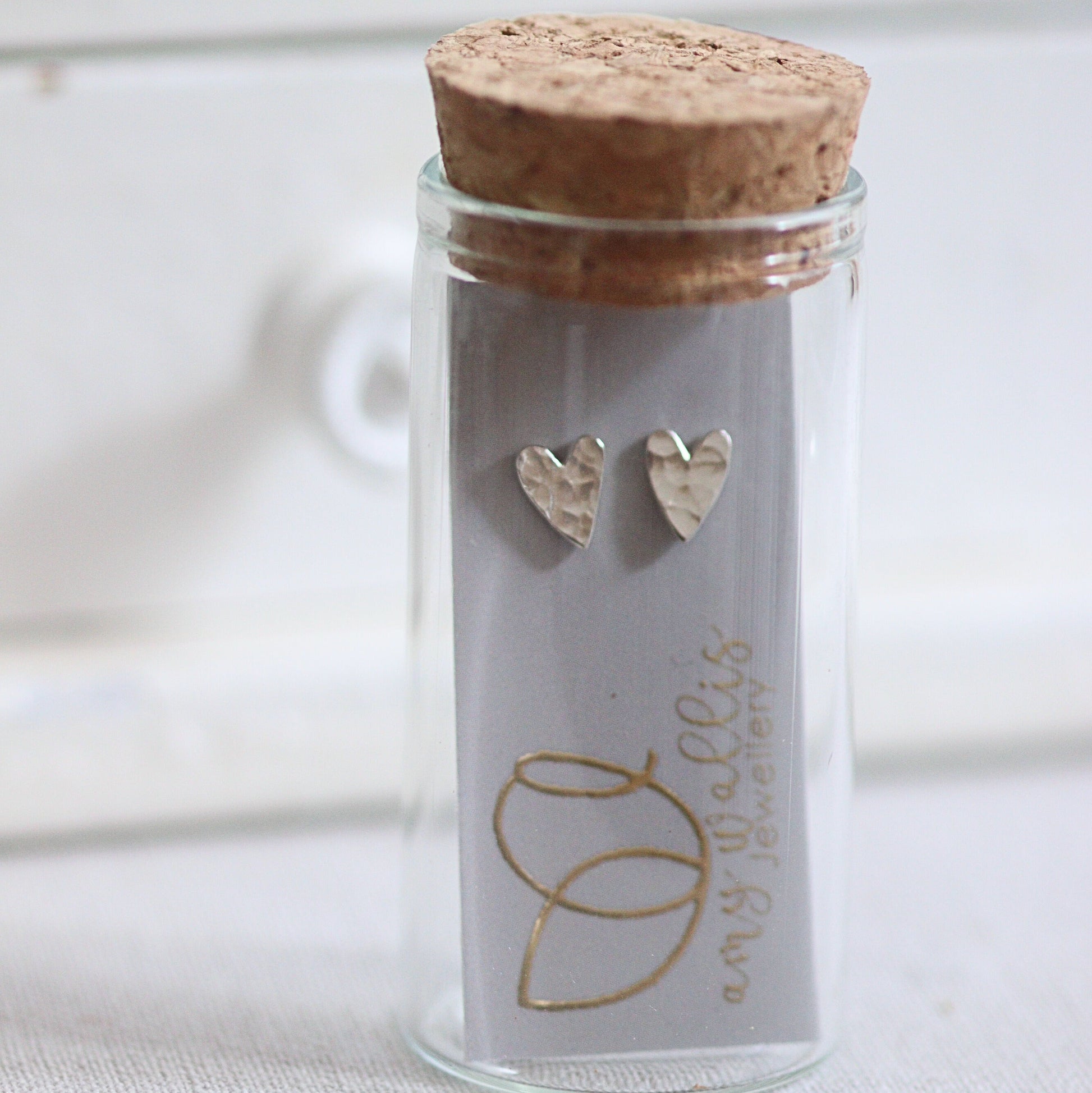 Glass jar with cork lid containing heart-shaped earrings on a white background