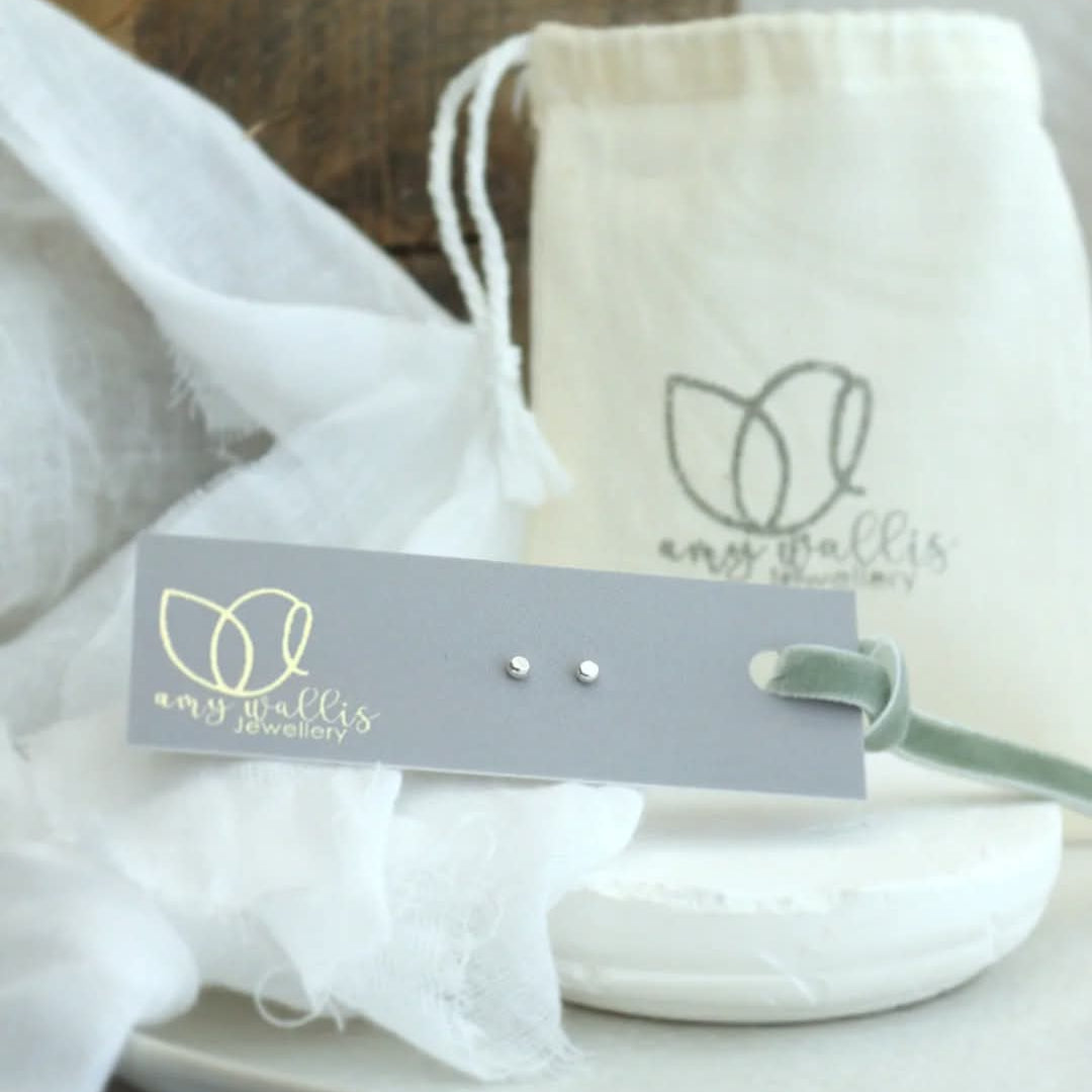 Earring set with branded card and pouch on a white surface