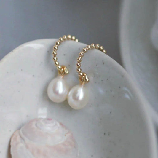Pearl earrings with gold hoops with a beaded bubble texture on a ceramic surface