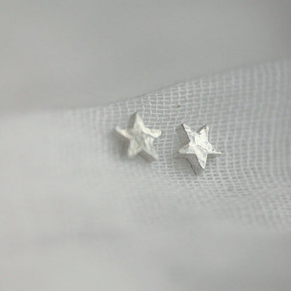 Side view of chunk silver star studs with a hammered texture. Threaded through fine muslin.