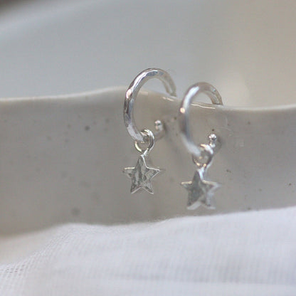 Silver hoop earrings with star charms on a white surface