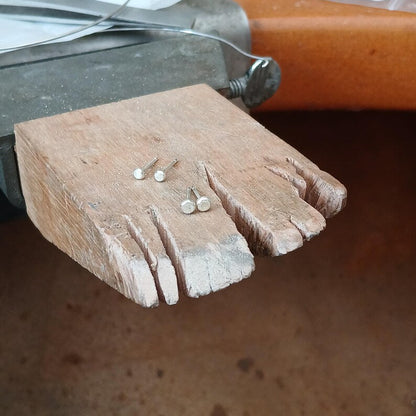 Wooden jewellers bench peg with tiny white gold stud earrings being made