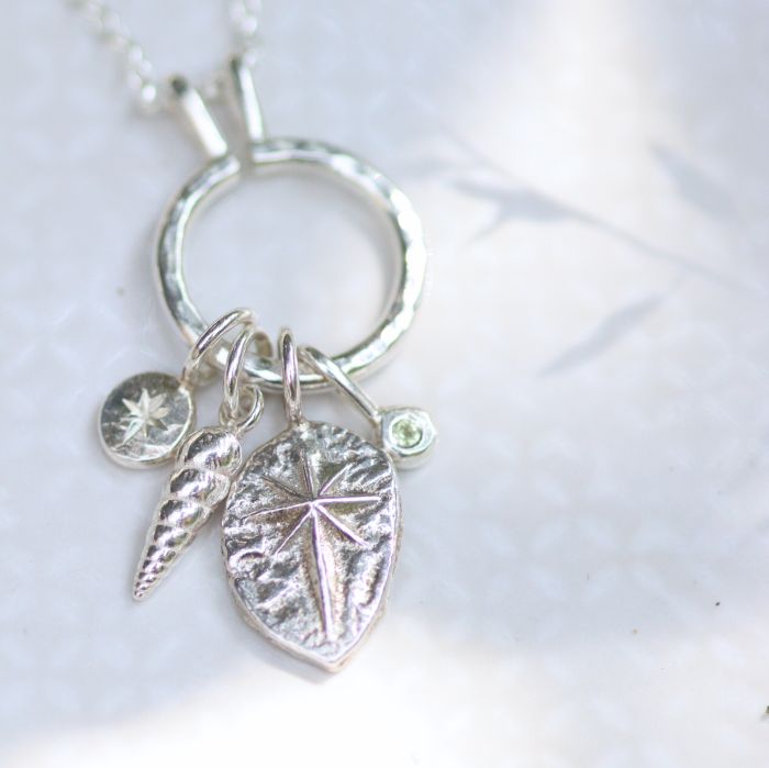 A silver keeper charm necklace with 4 different charms held on the pendant inluding a cast silver north star charm.