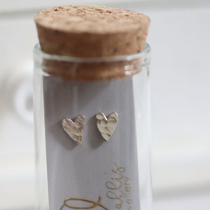 Heart-shaped silver earrings in a glass jar with cork lid on a white background