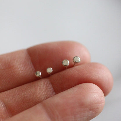 Four small white gold dot studs on a person's finger against a light background