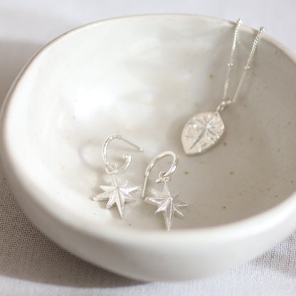 a little ceramic bowl with silver north star necklace and huggie earrings held inside.
