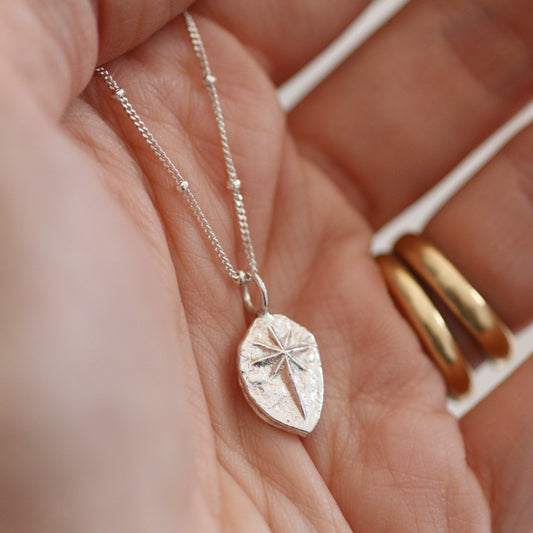 A solid silver north star pendant held n the palm of a hand on a beaded satellite silver chain. 