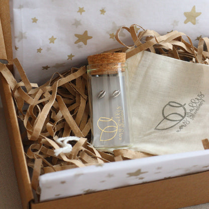 Oxidised tiny cowrie shell stud earrings presented in a glass bottle in a gift box with decorative tissue.