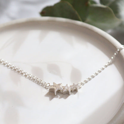 Silver star necklace on a white ceramic dish with green leaves in the background
