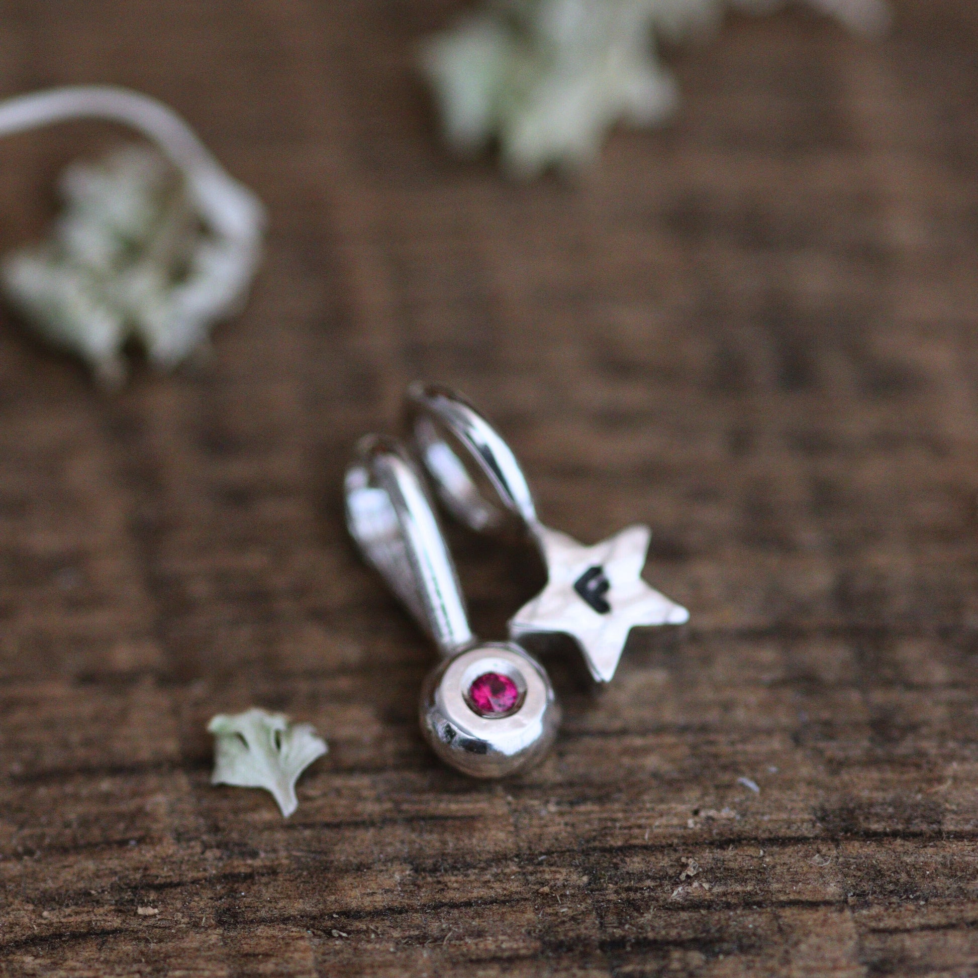 A red birthstone pendant and star pendant on a wooden background.